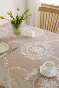 Detail einer warmbeigen Tischdecke mit Blumen-Spitze auf einem Holztisch mit Deko