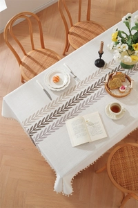 Detail of embroidered leaf patterns and handmade fringe on ivory rectangular tablecloth