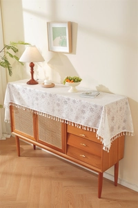 Close-up of white lace table runner with snowflake patterns and fringe on a wooden cabinet