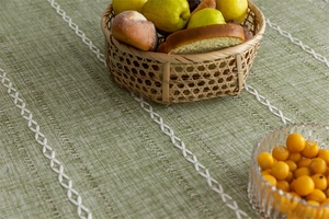 Close-up of green tablecloth showing woven texture and white geometric embroidery