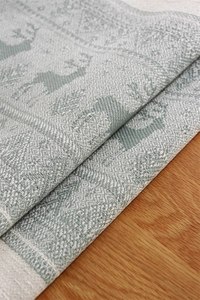 Detail of sage green jacquard table runner with winter reindeer and snowflake patterns