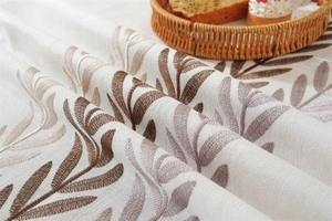 Detail of embroidered leaf patterns on beige linen tablecloth with rustic decor