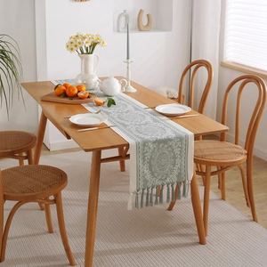 Green and cream bohemian jacquard table runner with decorative tassels on wooden table