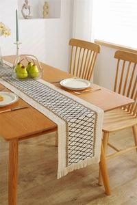Detail of woven table runner with black diamond pattern and fringe on wooden table