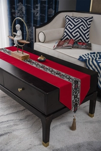 Macro detail of red table runner with floral embroidery and tassel on a dark coffee table