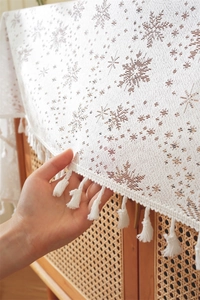 Close-up of French lace tablecloth featuring white snowflake patterns and tassel edges