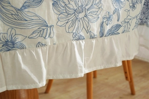 Detail of blue floral embroidery on white cotton tablecloth with elegant ruffled edge