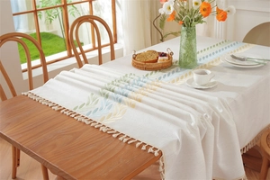 Macro detail of embroidered leaf patterns and white fringe tassels on linen tablecloth
