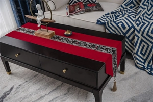 Detail of red Chinese style table runner with embroidery and tassels on a dark table