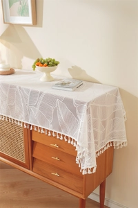 Close-up of cream lace table runner featuring leaf patterns and tassel fringe details