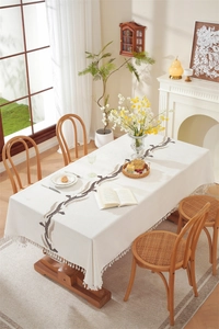 Detail of embroidered leaf patterns and white tassels on a beige waterproof tablecloth