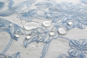 Macro shot of waterproof cotton fabric with blue floral embroidery and water droplets