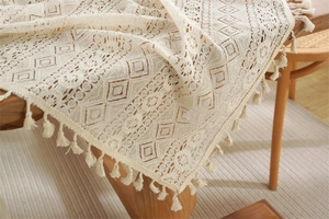Detail of beige lace table runner with geometric crochet patterns and elegant fringe tassels
