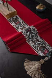 Macro detail of dark red Chinese table runner with floral embroidery and gold tassels