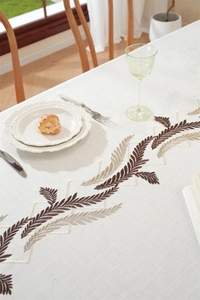 Detailed embroidery of brown leaves on beige cotton linen tablecloth with tassel edges