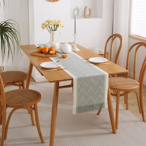 Green and cream geometric jacquard table runner with handmade tassels on wooden dining table