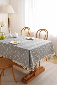 Close-up of bohemian grey tablecloth featuring white geometric patterns and cotton tassels
