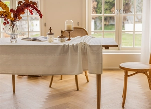 Close-up detail of cream rectangular tablecloth with elegant striped embroidery texture