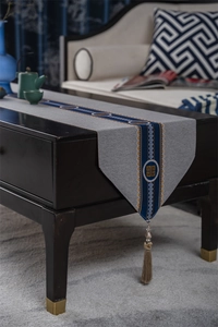 Detail of grey polyester table runner with blue embroidery and long tassel ornament