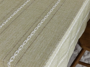 Detailed close-up of light green jacquard tablecloth with white leaf embroidery and cutouts