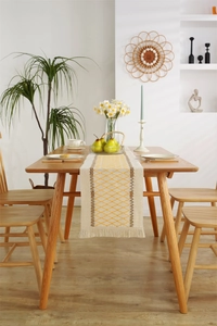 Detail of woven table runner with yellow diamond pattern and cream fringe on wooden table