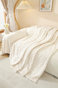 Close-up of plush cream sofa blanket with textured diamond knit pattern and soft lighting