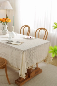 Close-up of beige hollow lace tablecloth with elegant fringe trim and geometric pattern
