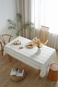 Close-up of white rectangular tablecloth with textured stripes and fringe on a wooden table