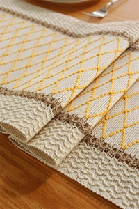 Detail of bohemian cotton linen table runner with yellow embroidery and brown woven trim