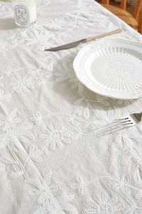Close-up of white floral embroidery on a cotton tablecloth with elegant table settings