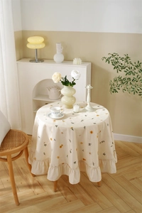 Detail of apricot cotton tablecloth featuring floral embroidery and ruffled edges