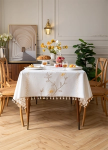 Close-up of cream embroidered floral tablecloth with elegant tassel fringe and textured fabric