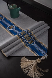Detail of grey table runner featuring blue and yellow embroidery and elegant beige tassels