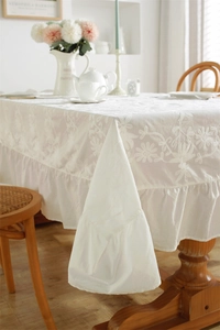 Macro shot of French style white tablecloth featuring delicate floral embroidery and ruffled edges