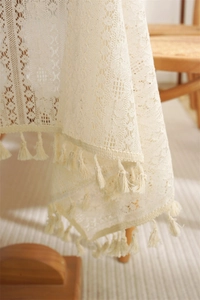 Close-up of beige lace tablecloth with geometric hollow patterns and decorative fringe