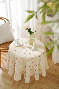 Detail of apricot cotton tablecloth with yellow daisy floral embroidery and ruffled hem