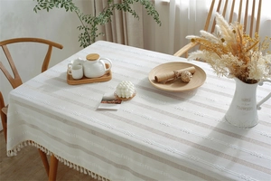 Close-up of beige jacquard tablecloth with textured stripes and elegant fringe edges