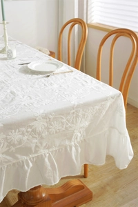 Detailed close-up of French floral embroidery and elegant ruffle hem on white cotton tablecloth