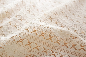 Close-up detail of beige lace fabric with hollow geometric patterns and tassels