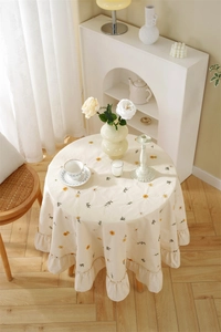 Detailed close-up of apricot cotton tablecloth with yellow daisies and ruffle edges