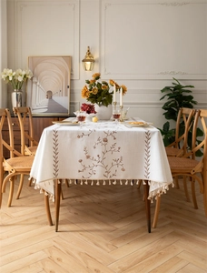 Close-up of beige linen tablecloth featuring floral embroidery and elegant fringe tassels