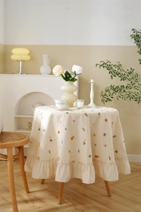 Detailed close-up of embroidered daisy patterns and ruffled edges on apricot cotton tablecloth