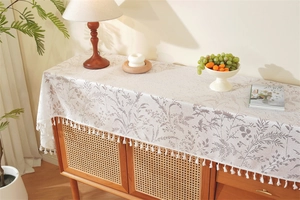Close-up of French lace table runner with grey leaf patterns and white fringe tassels