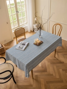 Detailed view of gray-blue rectangular tablecloth with white chain embroidery on wood table