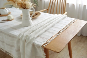 Close-up of beige woven tablecloth with hollow jacquard texture and decorative tassel edges