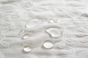 Close-up of waterproof embroidered cotton tablecloth showing hydrophobic water droplets