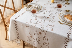Close-up of embroidered coffee leaf pattern and tassel edge on a beige tablecloth
