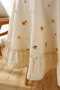 Detailed embroidery of yellow daisies on a ruffled apricot cotton tablecloth