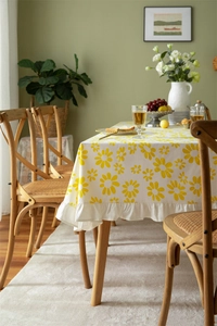 Close-up of white cotton tablecloth featuring yellow daisy prints and ruffled edge detail