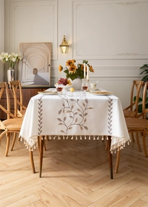 Detailed view of beige tablecloth with brown leaf embroidery and white ball tassel edges
